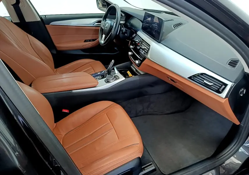 Vue intérieure côté conducteur de la BMW Série 5 Touring 530e 2022 avec sièges cuir marron et tableau de bord moderne.