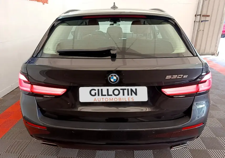 Vue arrière d’une BMW Série 5 Touring 530e gris clair avec feux LED allumés et logo visible sur coffre.