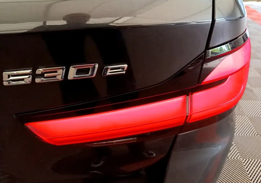 Gros plan sur le feu arrière droit rouge et le badge 530e d'une BMW Série 5 Touring gris foncé.