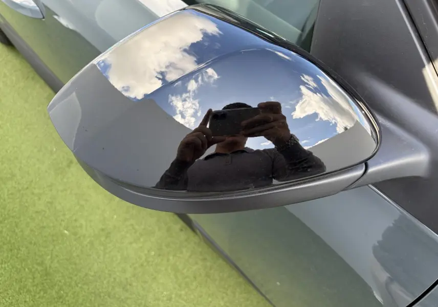 Rétroviseur extérieur droit noir brillant sur Citroën C5 Aircross vert Astoria avec reflet du ciel et d'une personne.