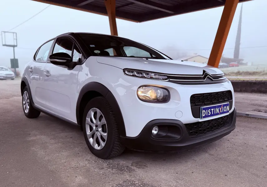Vue 3/4 avant gauche d'une Citroën C3 Société blanche de 2019 avec calandre noire et phares allumés.