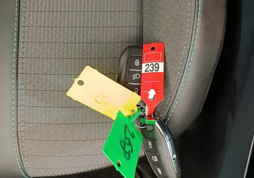 Gros plan sur la clé de Peugeot 208 posée sur un siège tissu gris avec surpiqûres bleues, intérieur sombre.