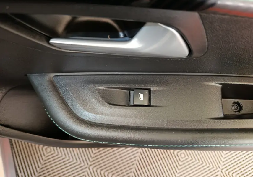Gros plan sur la poignée intérieure et le bouton de lève-vitre côté conducteur de la Peugeot 208 2020, finition noire.