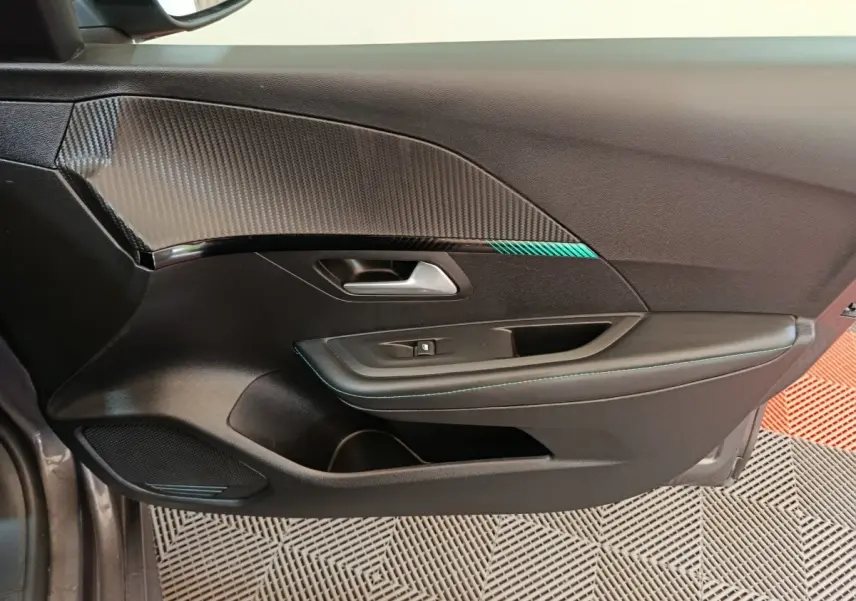 Vue rapprochée de la porte intérieure côté conducteur de la Peugeot 208 2020 avec insert carbone et surpiqûres bleues.
