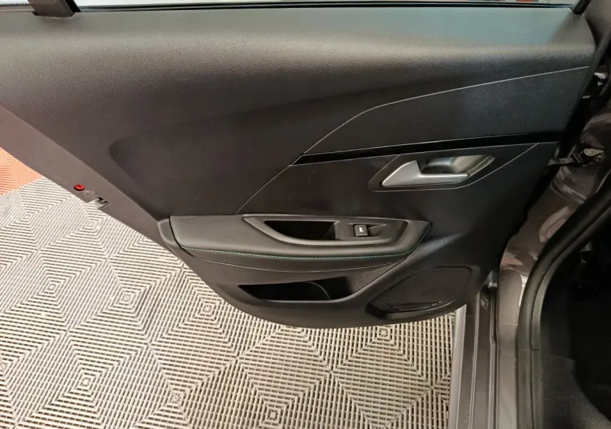 Vue latérale du panneau de porte arrière gauche noir avec poignée argentée et commande de fenêtre sur Peugeot 208.