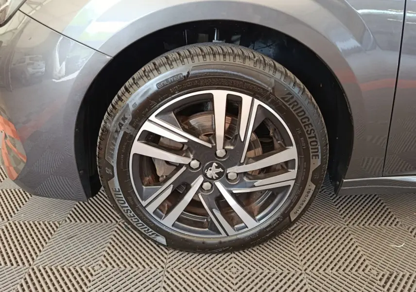 Gros plan sur la roue avant gauche grise d'une Peugeot 208 avec jante alliage et logo lion central.