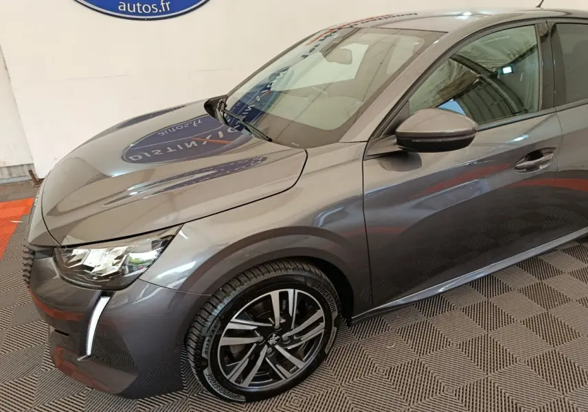 Vue 3/4 avant droit d'une Peugeot 208 gris métallisé avec phares LED et jantes alliage distinctives.