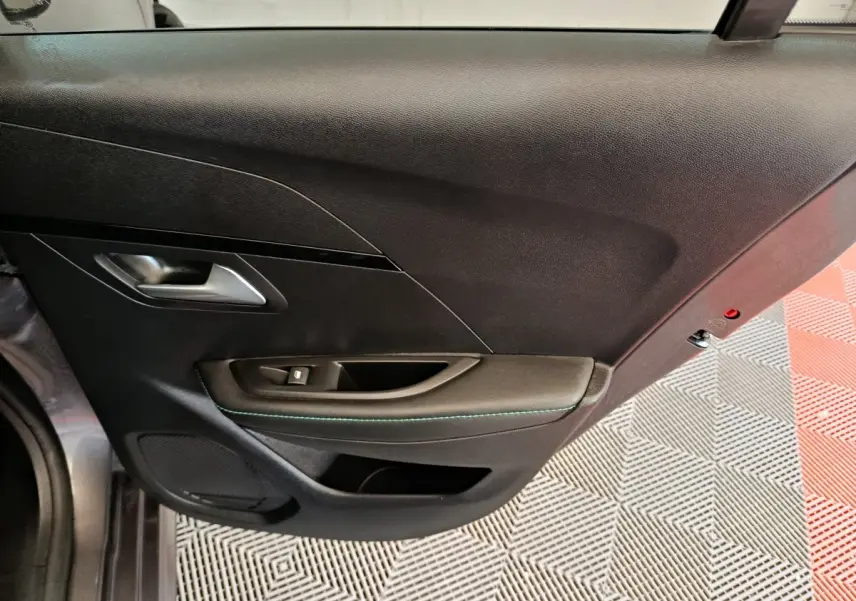 Vue rapprochée du panneau de porte intérieur côté gauche de la Peugeot 208 2020, finition noire avec surpiqûres vertes.