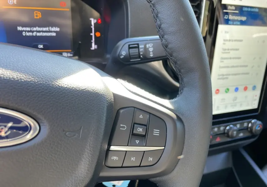 Gros plan sur le volant cuir du Ford Ranger gris iconic avec commandes multifonctions et écran tactile visible en arrière-plan.