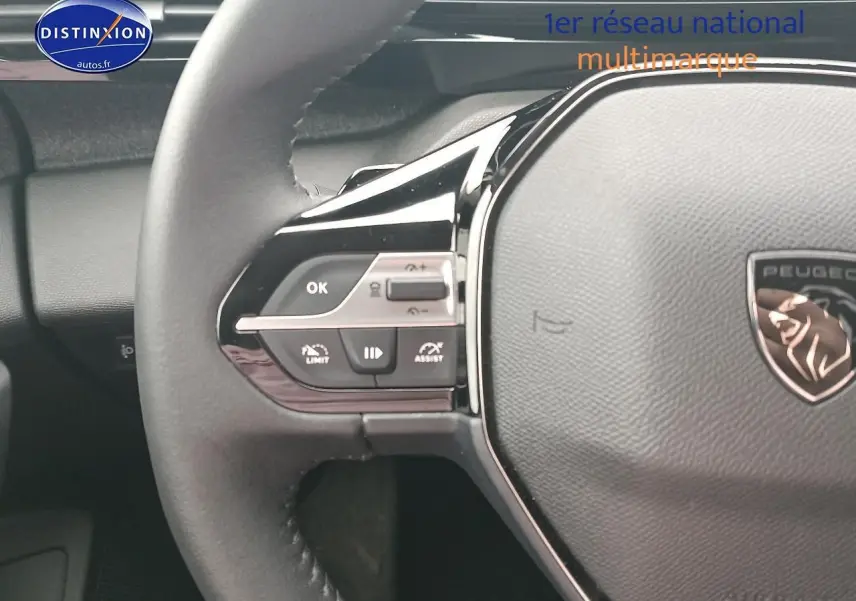 Gros plan sur le volant cuir multifonction gris d’une Peugeot 408 Hybrid 145 allure 2024 avec commandes intégrées côté gauche.
