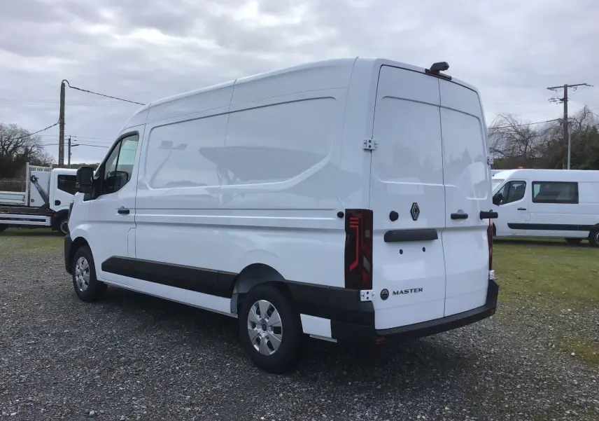 Vue 3/4 arrière droite d’un Renault Master blanc, fourgon utilitaire avec portes arrière fermées sur un sol gravillonné.
