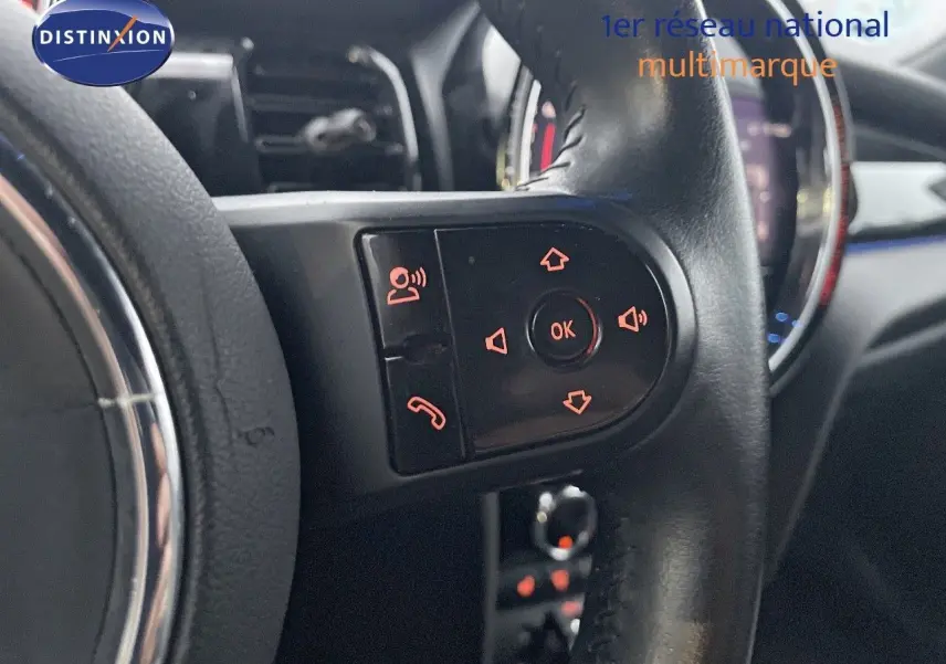 Gros plan sur les commandes du volant noir de la MINI Cabriolet F57 rouge chili, avec boutons rétroéclairés orange.