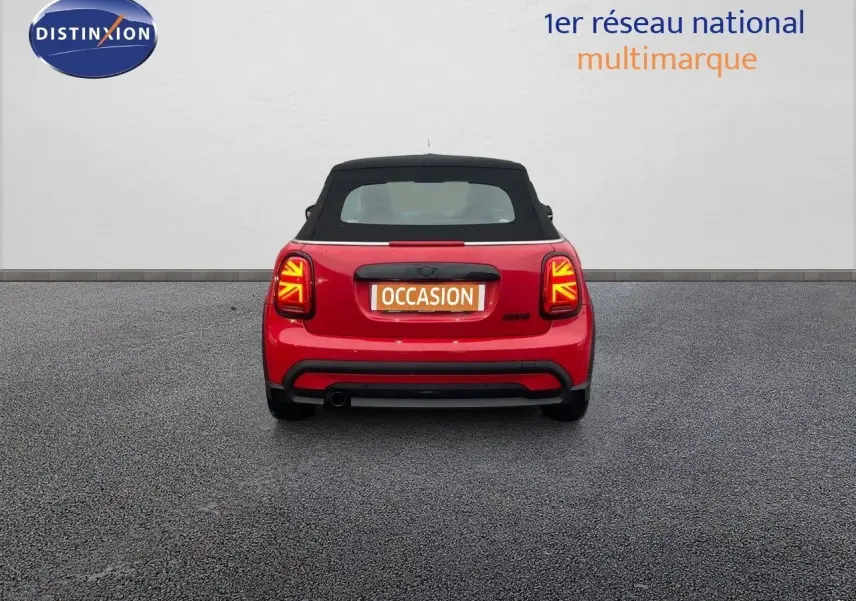 Vue arrière d'une MINI Cabriolet F57 rouge chili avec capote noire et feux arrière à motif Union Jack allumés.