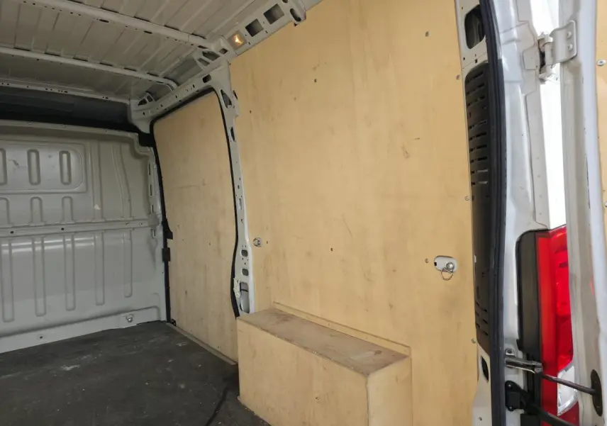 Intérieur du fourgon Opel Movano blanc vu de l'arrière, avec panneaux latéraux et plancher en bois clair.