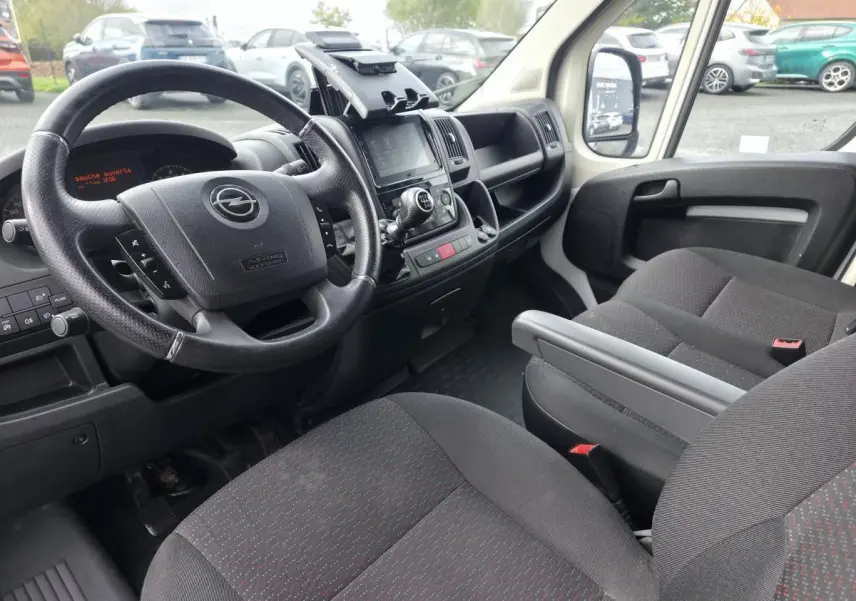 Intérieur de l’Opel Movano Fourgon 2022 vu côté conducteur, avec volant noir et sièges tissu gris foncé à motifs rouges.