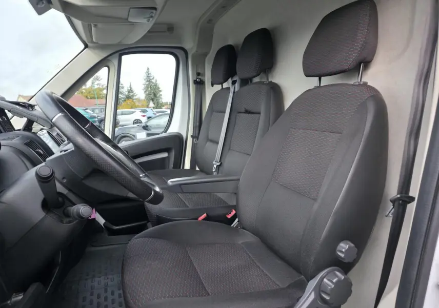 Vue intérieure côté conducteur de l'Opel Movano blanc, montrant les sièges en tissu gris foncé et le volant noir.