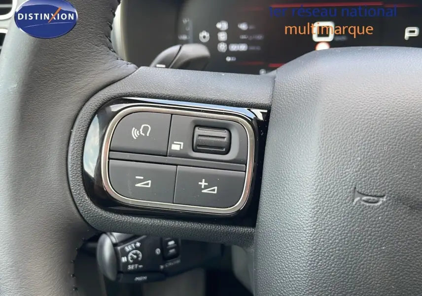 Gros plan sur les commandes au volant noir du Citroën C5 Aircross 2025 blanc, avec tableau de bord numérique en arrière-plan.