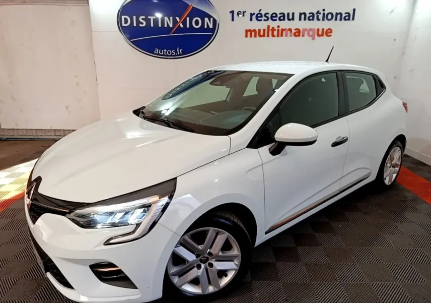 Renault Clio Business blanc vue 3/4 avant droit, feux LED allumés, dans showroom avec logo Distinxion en arrière-plan.