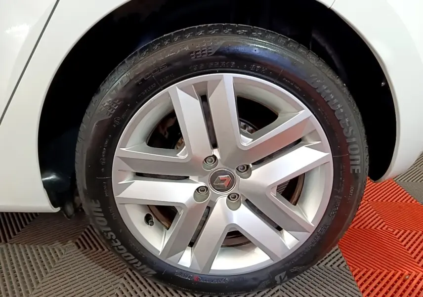 Gros plan sur l'aile arrière blanche de la Renault Clio Business SCe 65, avec partie de la roue visible sur sol carrelé rouge et gris.