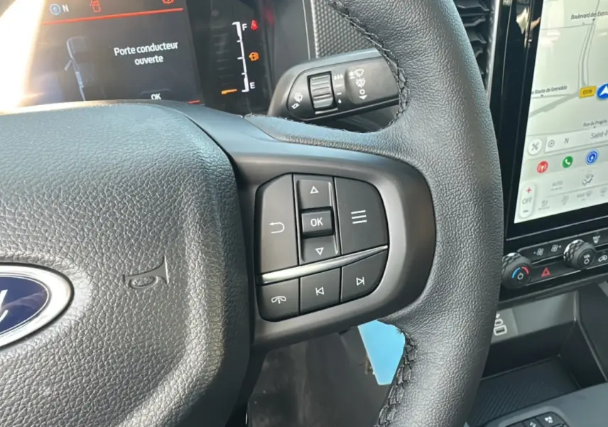 Gros plan sur le volant cuir noir du Ford Ranger 2026 avec commandes multifonctions et écran tactile visible à droite.