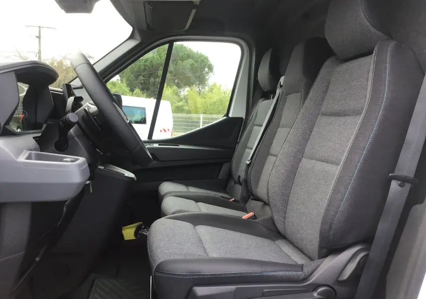Vue intérieure côté gauche du Renault Master 2026, montrant les sièges gris avec surpiqûres bleues et le volant.