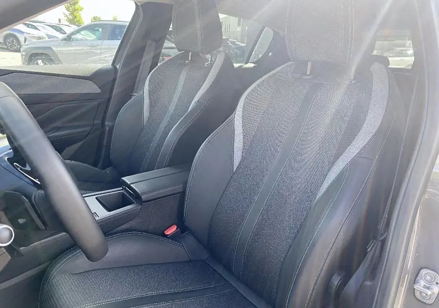 Vue intérieure sur les sièges avant en tissu et cuir noir de la Peugeot 308 gris, avec accoudoir central et volant multifonction.