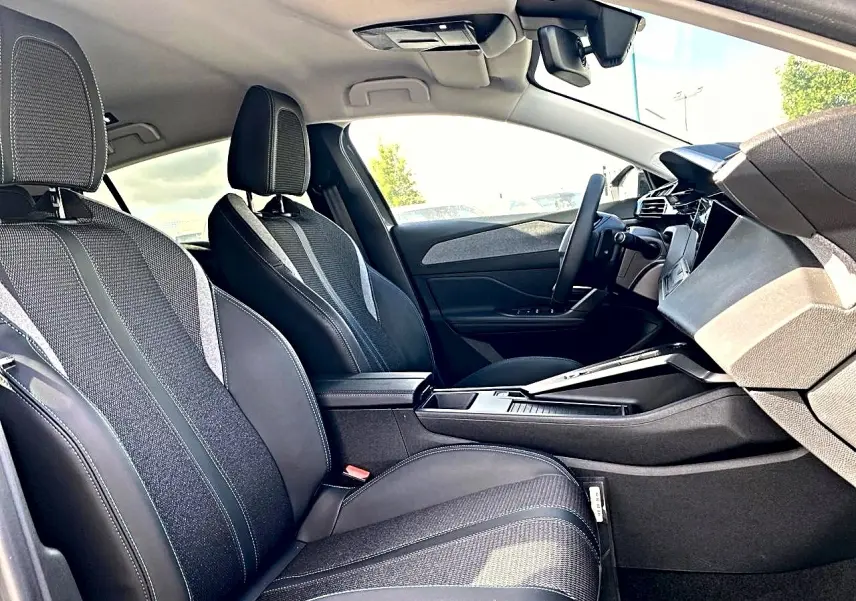 Vue intérieure côté conducteur de la Peugeot 308 2025, sièges noirs avec tissu et cuir, console centrale moderne.