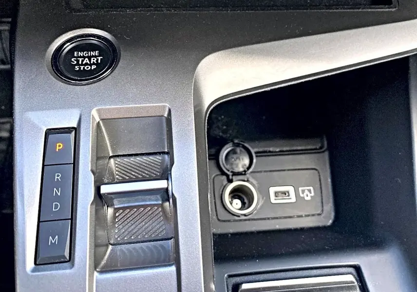 Gros plan sur la console centrale grise de la Peugeot 308 2025 avec bouton start/stop, levier de boîte auto et prises USB/12V.