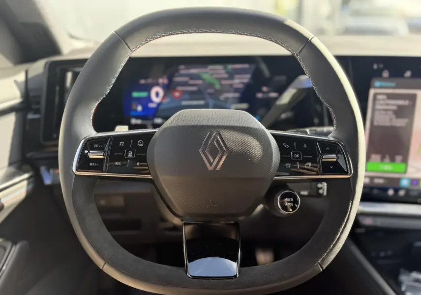 Volant Alcantara avec surpiqûres tricolores et logo Renault, tableau de bord numérique flou en arrière-plan