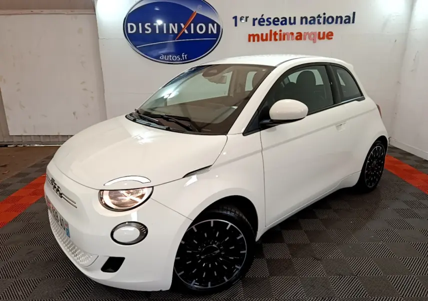Fiat 500 électrique blanche vue 3/4 avant droit, avec phares allumés et jantes noires stylisées.
