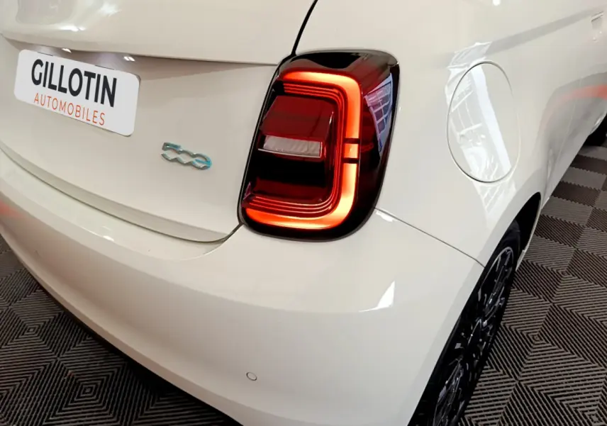 Vue 3/4 arrière droite d'une FIAT 500 blanche électrique avec feu arrière LED distinctif et logo 500 bleu.