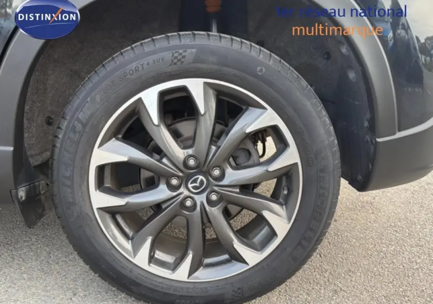 Gros plan sur la jante alliage 19 pouces gris foncé du Mazda CX-5 noir, mettant en valeur le logo Mazda central.