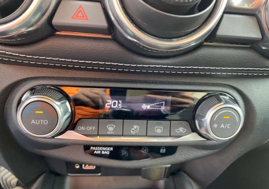Détail de la console de climatisation automatique du Nissan Juke blanc perle 2024 avec affichage digital et commandes rotatives.