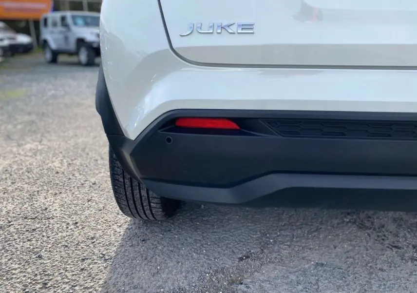 Gros plan sur l'arrière gauche d'un Nissan Juke blanc perle 2024, mettant en valeur le logo et le pare-chocs noir.
