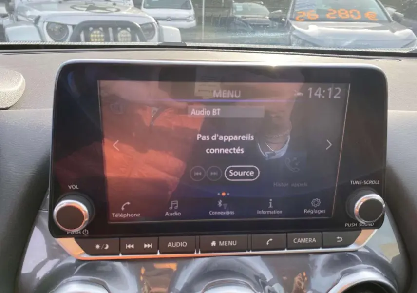 Écran tactile multimédia du Nissan Juke 2024 blanc perle, vue intérieure centrée sur la console avec commandes audio et caméra.