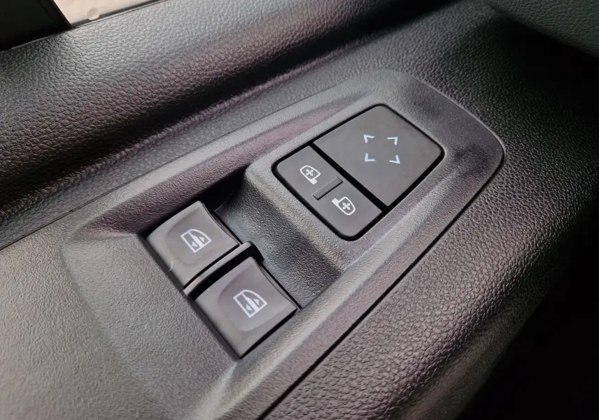 Gros plan sur les commandes de réglage des vitres et des rétroviseurs sur la porte intérieure noire du Renault Master gris urbain.