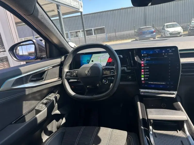 Vue intérieure avant du Renault Austral 2025, volant multifonction et grand écran tactile central lumineux.