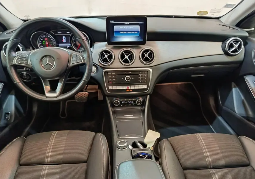 Vue intérieure frontale du tableau de bord et volant cuir noir d'une Mercedes GLA 220 d Business Exec 2018 avec écran central et aérateurs ronds.