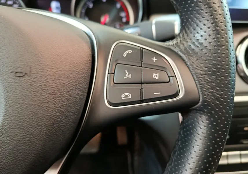 Gros plan sur les commandes audio et téléphone du volant cuir perforé côté gauche d'un Mercedes GLA noir de 2018.