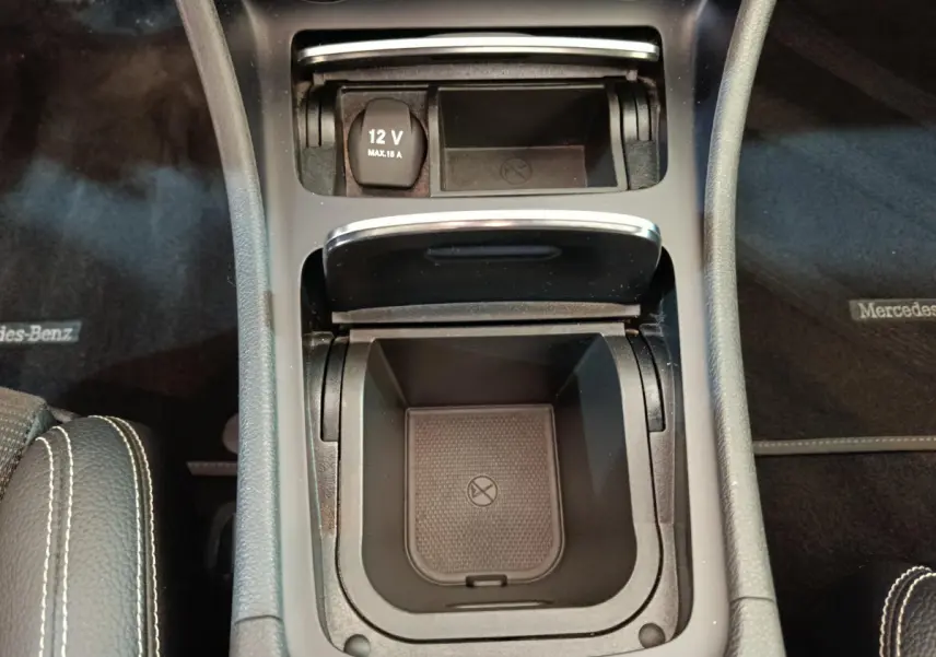 Vue plongeante sur la console centrale noire du Mercedes GLA 220 d, avec prise 12V et compartiment de rangement ouvert.