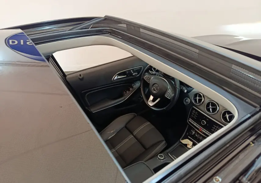 Vue intérieure par le toit ouvrant d'un Mercedes GLA noir, montrant le volant cuir multifonctions et le tableau de bord moderne.
