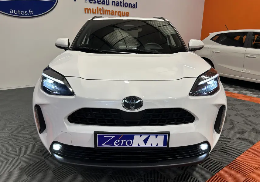 Vue avant d'une Toyota Yaris Cross blanche 2025 avec phares LED allumés et plaque Zéro KM visible.