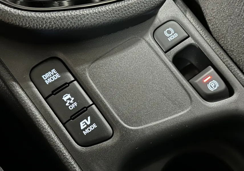 Gros plan sur les commandes de modes de conduite et frein à main électronique dans le Toyota Yaris Cross blanc 2025.