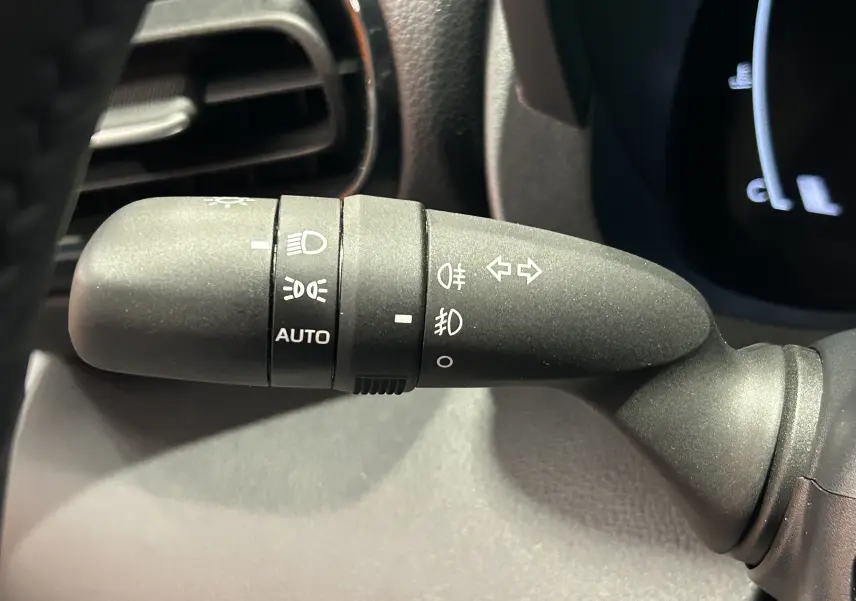 Gros plan sur la commande de feux noire à gauche du volant dans l'habitacle du Toyota Yaris Cross blanc 2025.