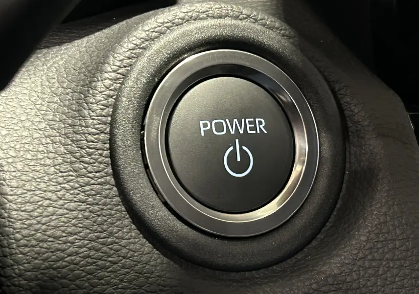 Bouton de démarrage Power en gros plan sur le tableau de bord noir de la Toyota Yaris Cross blanche hybride 2025.