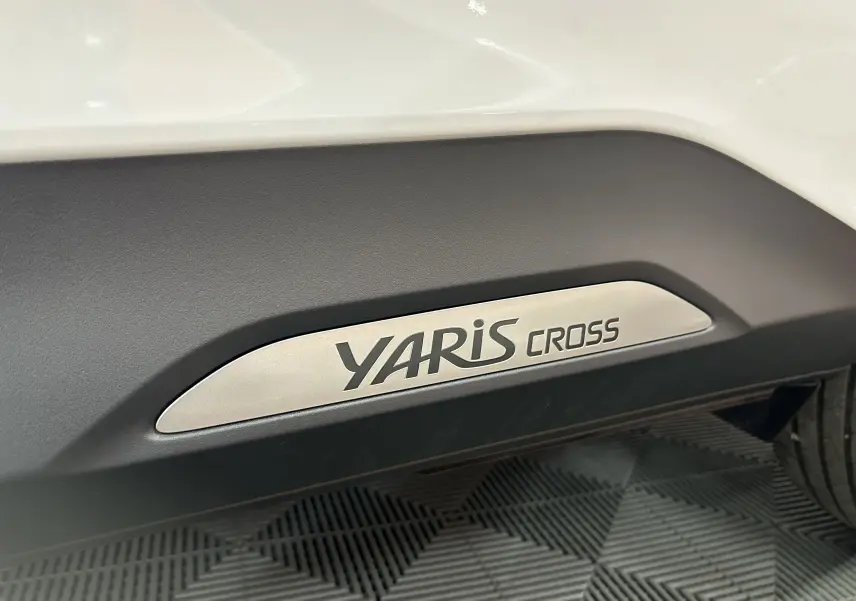 Gros plan sur l’inscription YARIS CROSS sur la bas de caisse noire d’un Toyota Yaris Cross blanc.