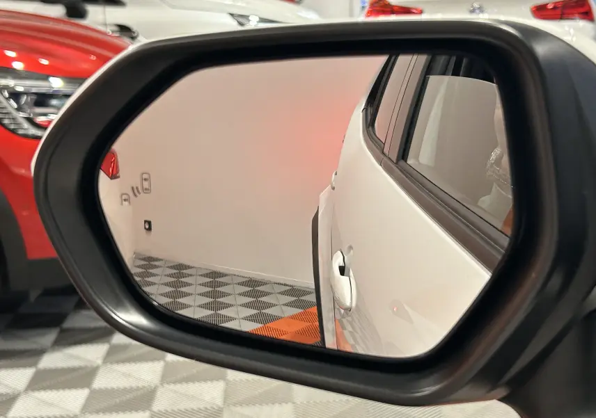 Rétroviseur gauche montrant la porte blanche d'une Toyota Yaris Cross 130 Design 2025 en intérieur showroom.