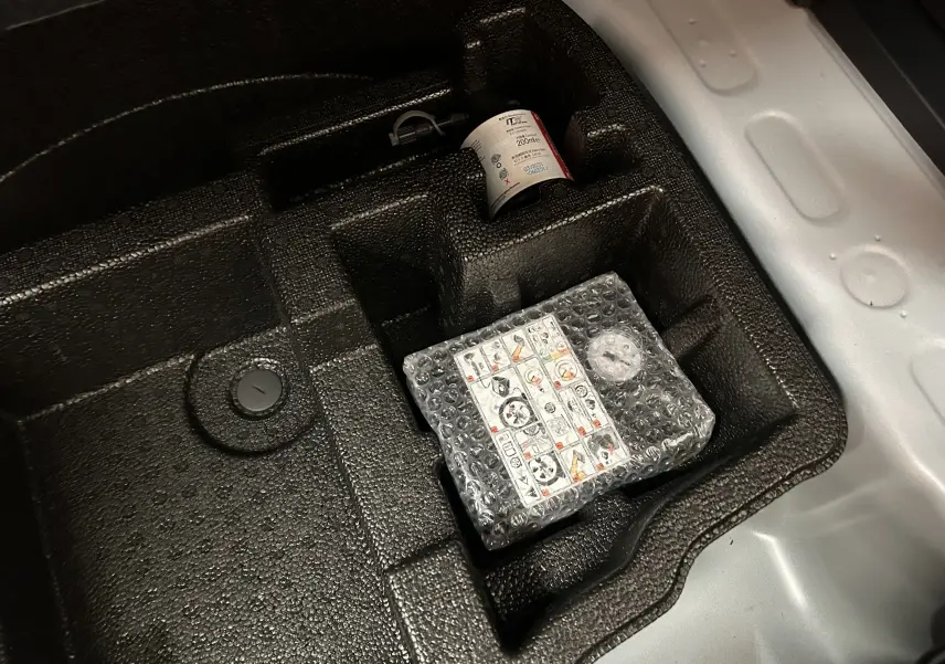 Gros plan sur le compartiment de rangement sous le plancher de coffre de la Toyota Yaris Cross blanche 2025, avec kit de réparation pneus.
