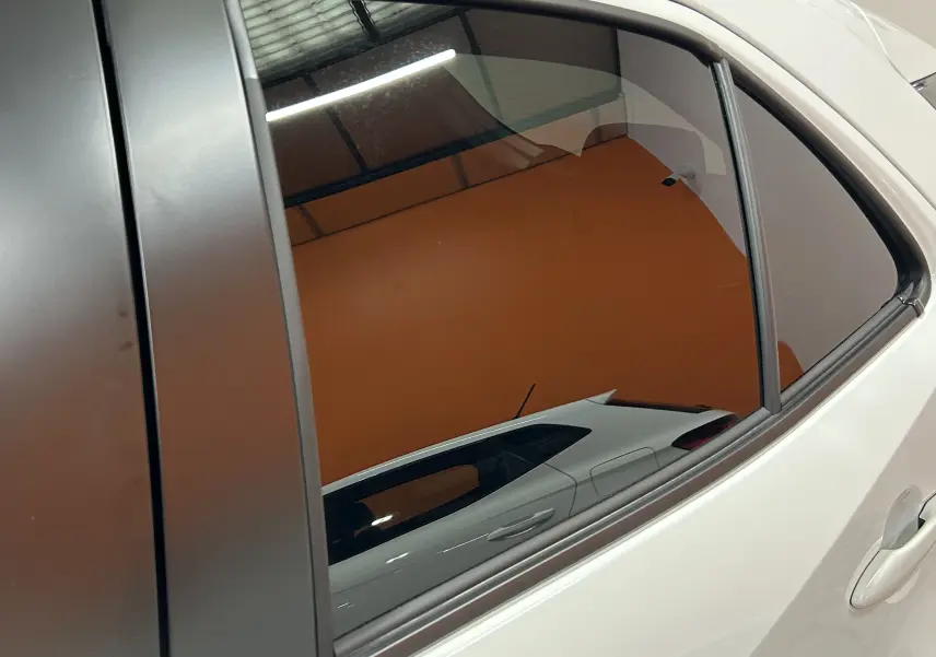 Reflet du profil arrière droit blanc d'une Toyota Yaris Cross 130 Design 2025 sur la vitre teintée du véhicule.