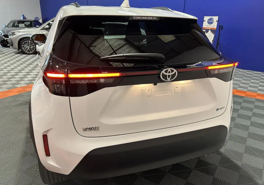 Vue arrière d'une Toyota Yaris Cross blanche avec feux arrière allumés dans un showroom intérieur.
